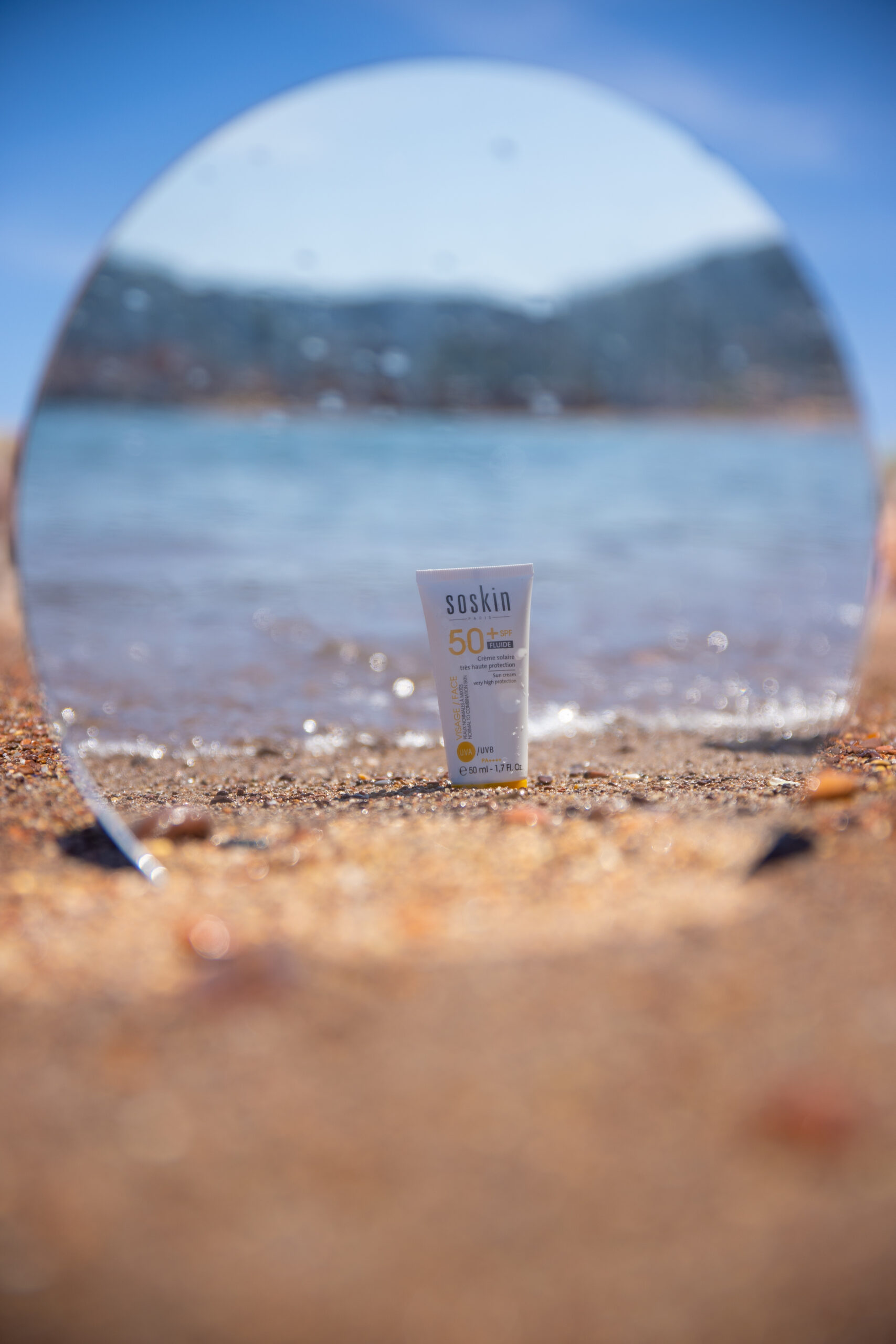 Crème solaire Soskin dans le reflet d'u miroir posé sur la plage